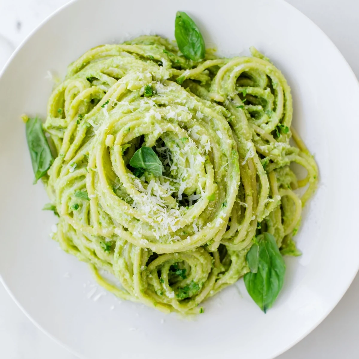Close-up of creamy avocado pasta, garnished with fresh basil and Parmesan cheese, ready to eat.