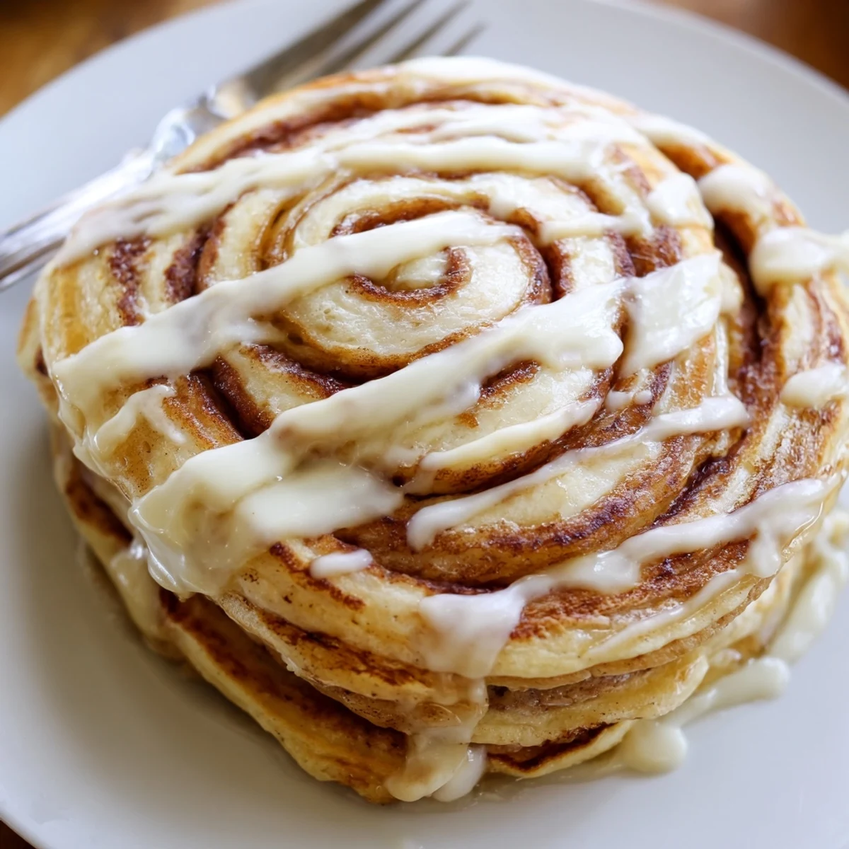 Golden Cinnamon Roll Pancakes, perfectly round, drenched in rich cream cheese glaze, ready to eat.