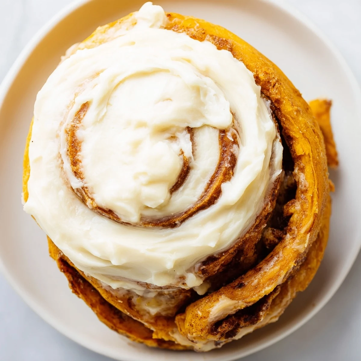 Freshly baked pumpkin cinnamon rolls with a generous drizzle of cream cheese frosting on a rustic wooden board.  