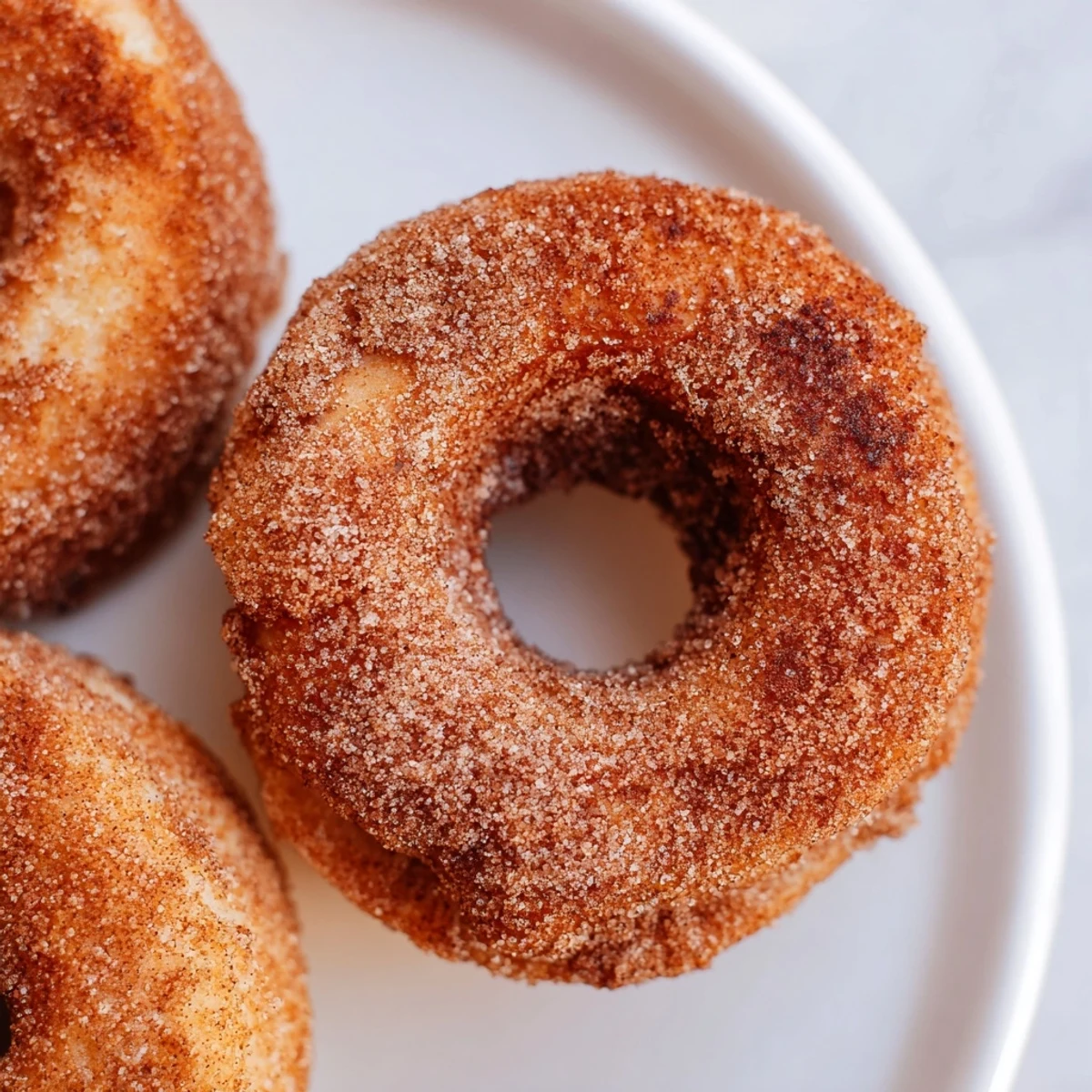 Fluffy Air Fryer Cinnamon Sugar Donuts, golden and coated in sweet spice, rest on a rustic plate with a cup of coffee.