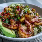 Smoky grilled shrimp and sliced avocado rest on quinoa, drizzled with tangy lime chili sauce in this bowl.