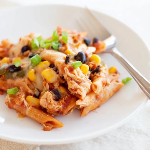 Steamy, melted cheese stretches from a spoonful of Chicken Enchilada Pasta, revealing tender penne noodles coated in red sauce.