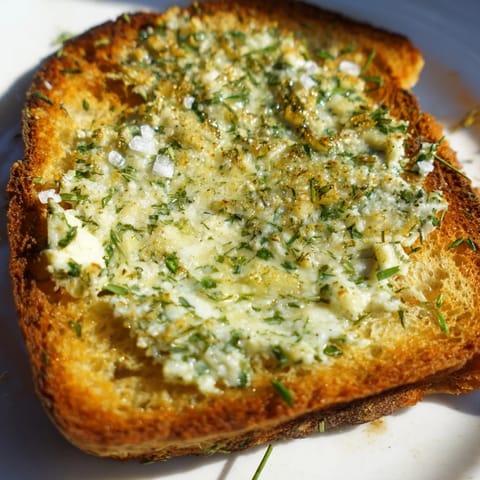 Freshly toasted bread slices topped with aromatic herb compound butter, sprinkled with sea salt beside a glass of white wine.  