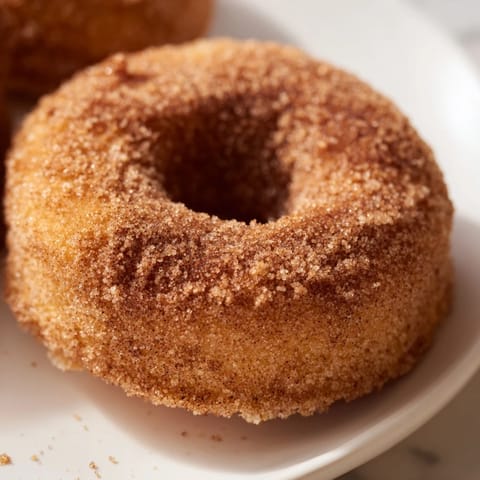Eight golden Air Fryer Cinnamon Sugar Donuts are arranged neatly, showing their puffy texture and glistening cinnamon sugar coating.