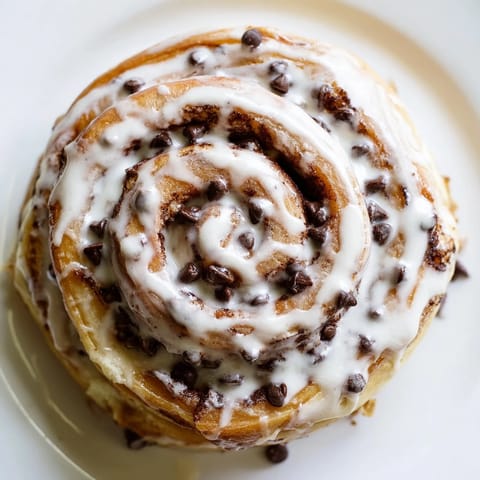 Freshly baked Nutella Chocolate Chip Rolls with a gooey center, served warm on a rustic plate with a drizzle of glaze.