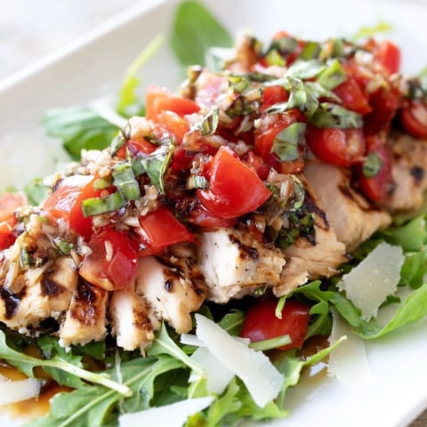 Juicy grilled chicken slices rest on crisp mixed greens, topped with a fresh bruschetta chicken salad of tomato, basil, and balsamic.