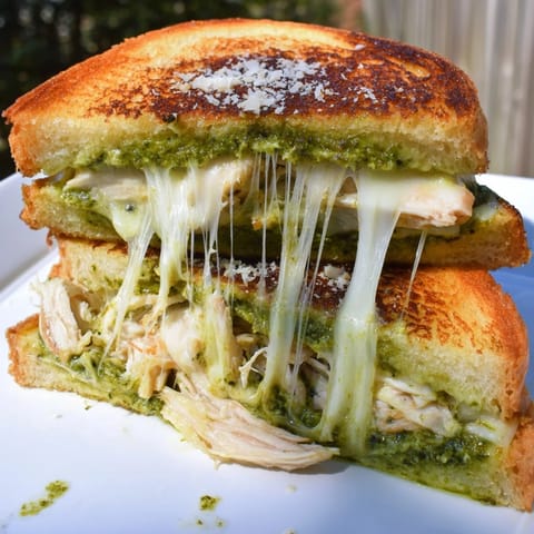 Golden toasted sourdough grilled cheese with shredded chicken, vibrant pesto, and melted mozzarella on a rustic plate.  