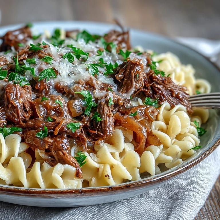 Hearty Crockpot French Onion Pot Roast Pasta served family-style, topped with melted Gruyère cheese and fresh parsley on a cozy dinner table.